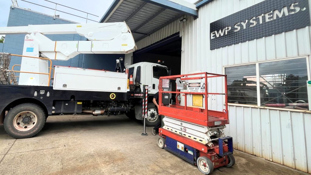 Truck-mounted EWP and scissor lift side by side at workshop showing different machine types
